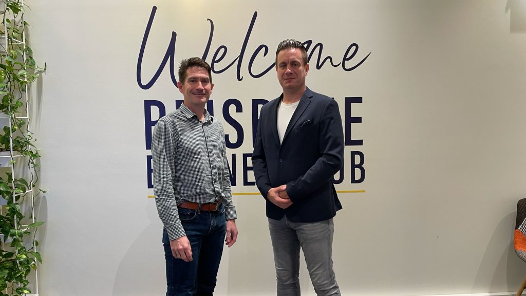 Matthew Clarkson and Simon Dell smiling in front of the Welcome Brisbane Business Hub sign
