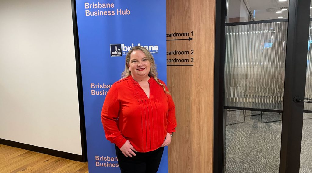 Blonde woman in a red top standing in front of the Brisbane Business Hub banner